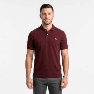 Man wearing a premium men's burgundy maroon polo shirt with a gold embroidered laurel wreath logo on the chest